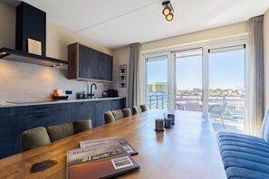 A modern kitchen with dark cabinets, a wooden dining table, and a view of a construction site through large windows.