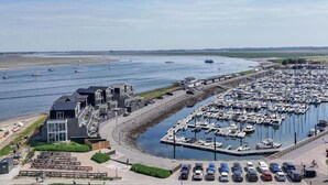 A marina with numerous boats docked, a building with a modern design, and a parking area with cars.