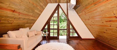 A cozy room with a wooden sloped ceiling, a white sofa, a round doily, and a small table with a plant.