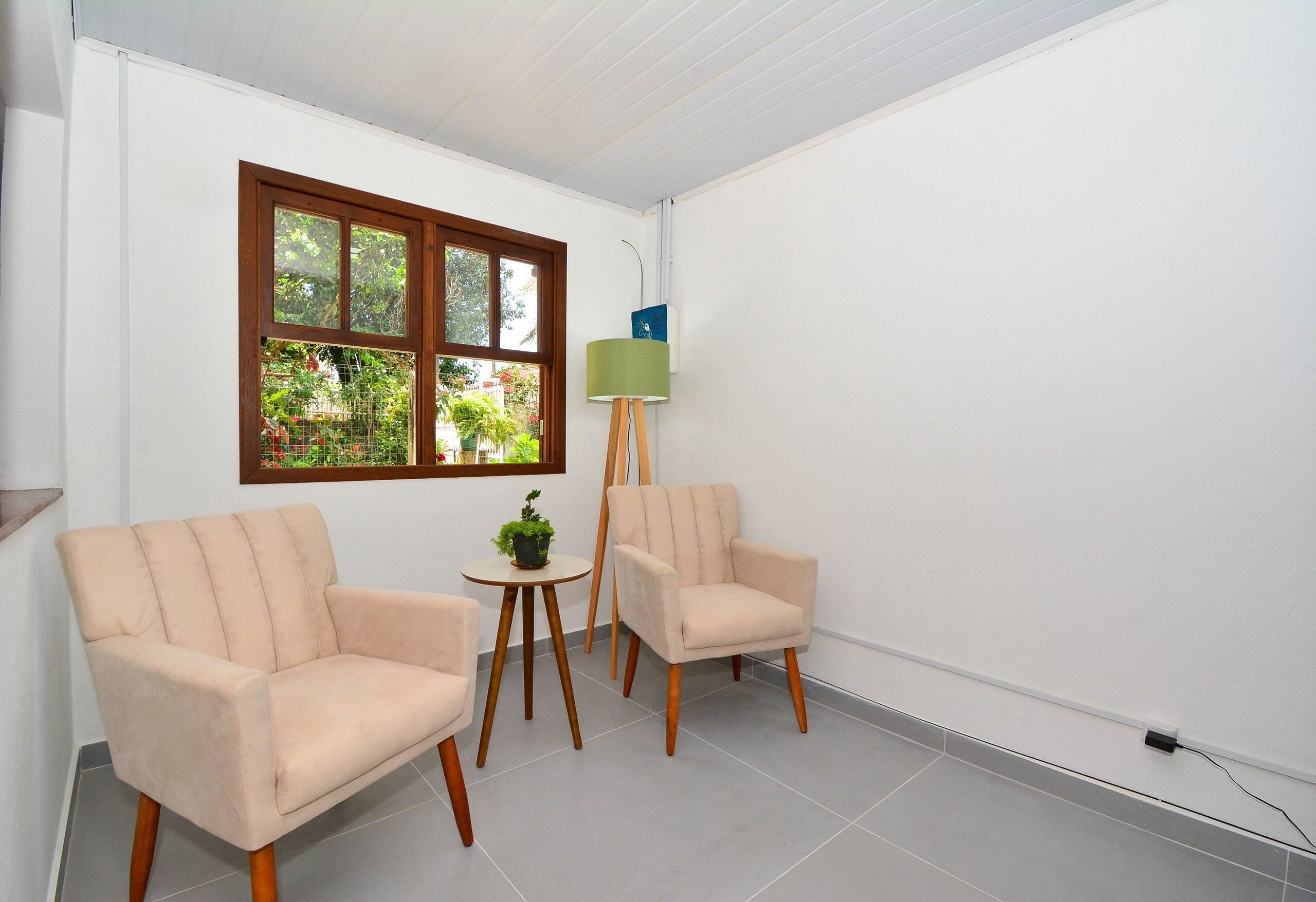 Um quarto com duas poltronas bege, uma mesa redonda pequena com uma planta e um abajur.