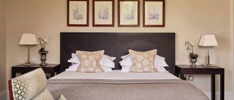 A neatly arranged hotel room with a large bed, two bedside tables, and a headboard. There are framed pictures on the wall above the bed.
