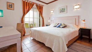 Un dormitorio con cama, escritorio, silla, mesita de noche y ventana con cortinas.