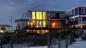Une maison située en bord de mer, avec plusieurs niveaux, un balcon et une cour clôturée.