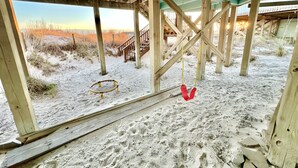 Une maison de plage dotée d’une terrasse en bois, d’une balançoire et offrant une vue sur la plage et les dunes.