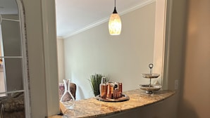 A kitchen with a marble countertop, two black barstools, a hanging pendant light, and a decorative mirror above the counter. - Come visit our “Sweet Retreat at the End of the Street” where you can relax!!! (Summerville)