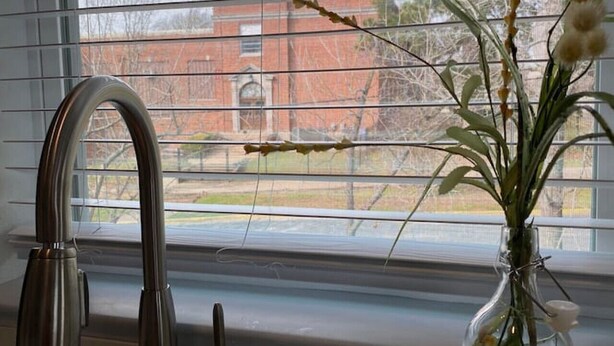 A kitchen with a stainless steel faucet and a vase of flowers on the windowsill. - Elizabeth Manor in Downtown Huntsville (Huntsville)