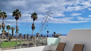 A rooftop terrace with lounge chairs, a view of the ocean, and palm trees.
