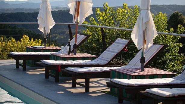 Zona junto a la piscina con sillones de descanso y sombrillas, con una vista despejada de las montañas al fondo.