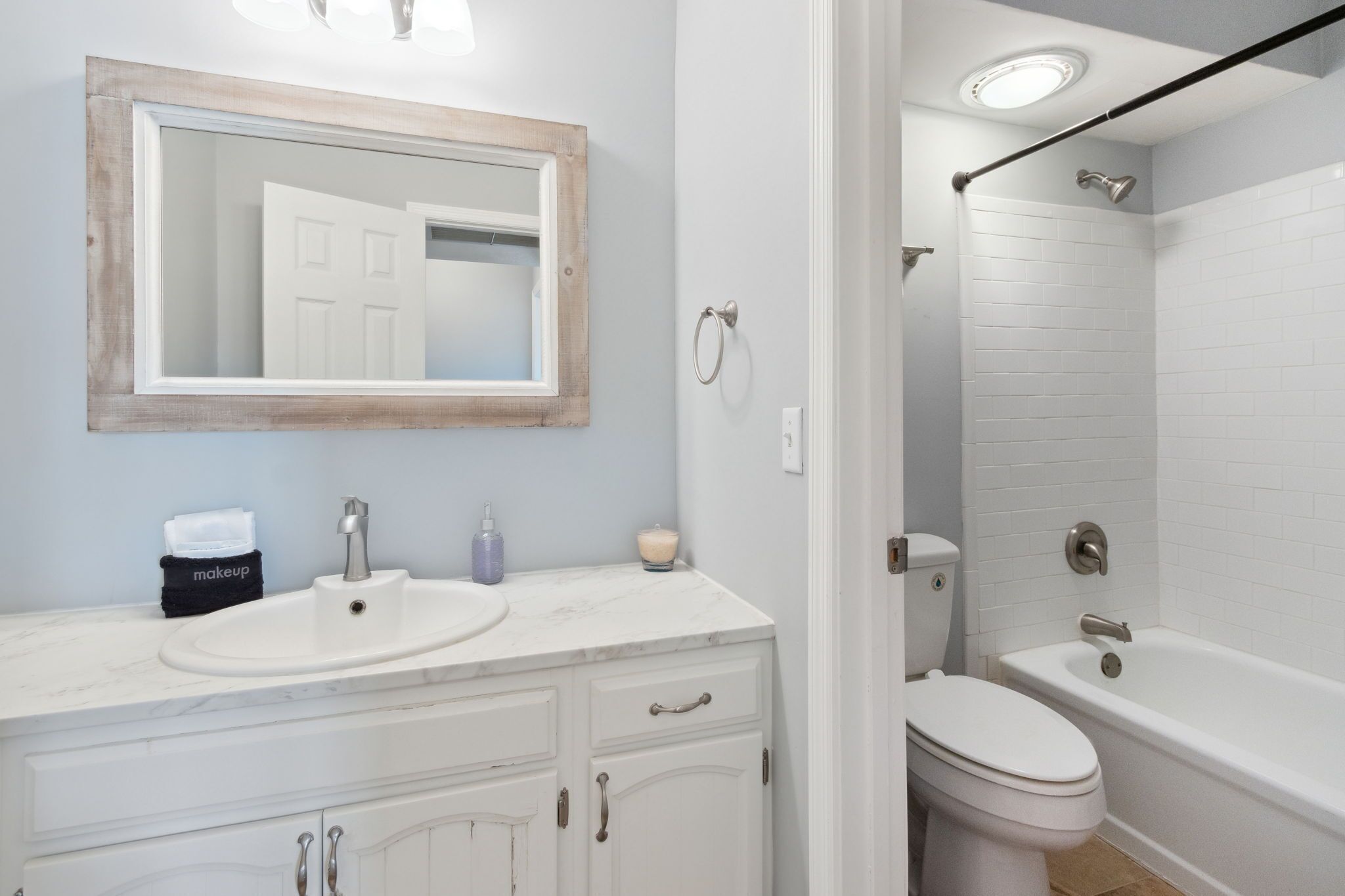A bathroom with a white sink, mirror, toilet, and bathtub.