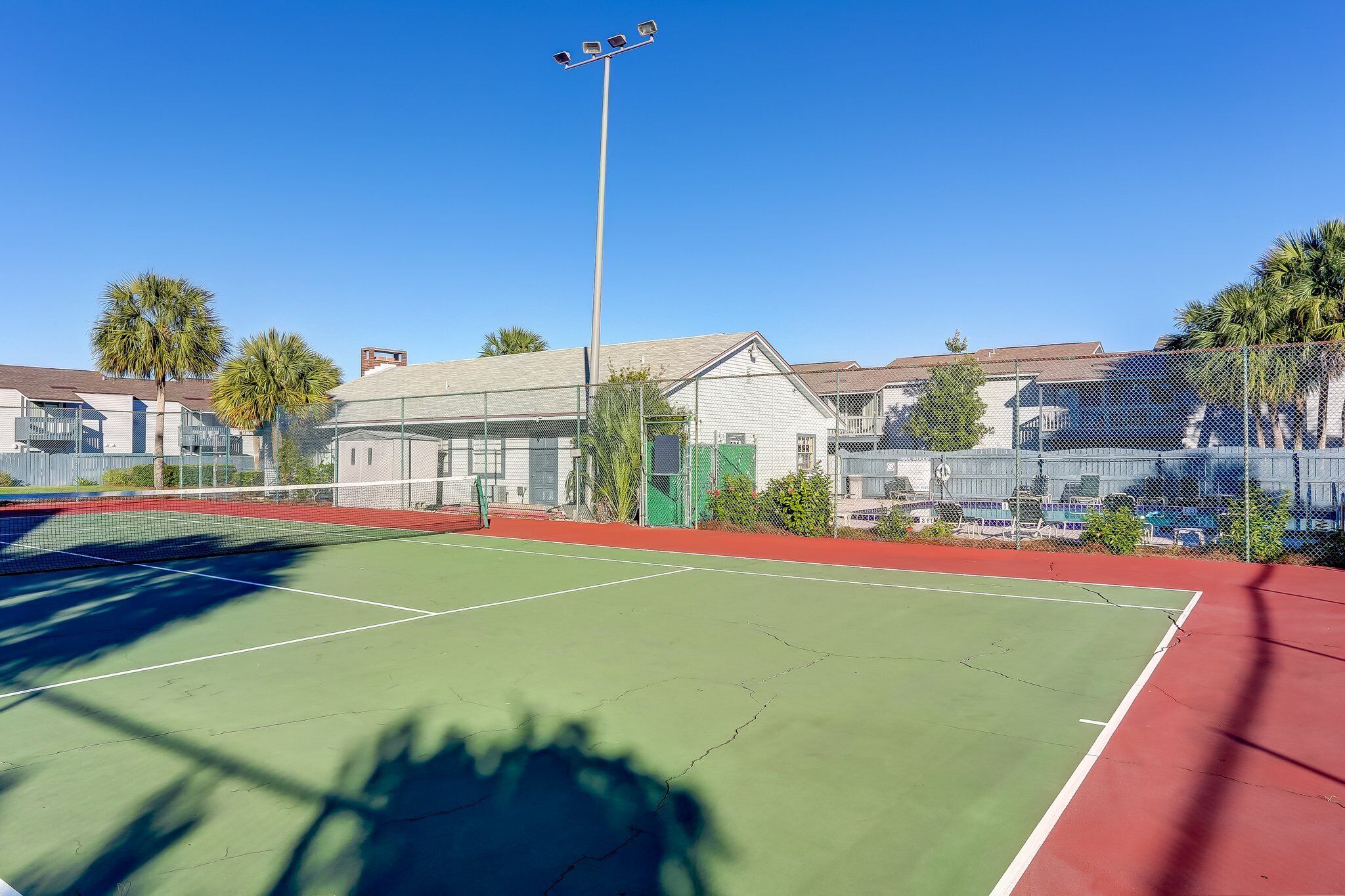 Un court de tennis avec un filet, entouré d’une clôture, et bordé de bâtiments.