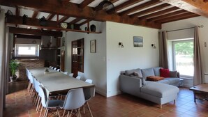 Zona d'estar àmplia amb taula de dinar, cadires, sofà i cuina al fons.