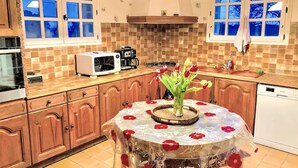 A kitchen with wooden cabinets, a microwave, a coffee maker, and a table with a floral tablecloth and tulips. - Bastide in Nîmes ⭐️⭐️⭐️ (Nîmes)