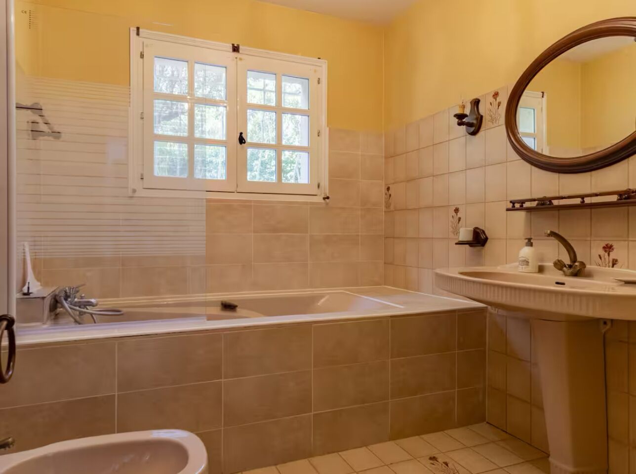 Ein Badezimmer mit einer Badewanne, einem Waschbecken, einem Spiegel und einem Fenster.