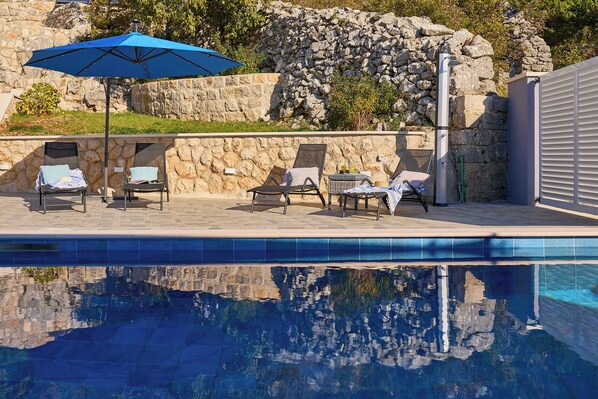 Ein Schwimmbecken mit Liegestühlen und einem blauen Sonnenschirm.
