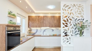 Una cucina moderna con mobili bianchi, elementi in legno e un pannello decorativo bianco con motivi a foglia.