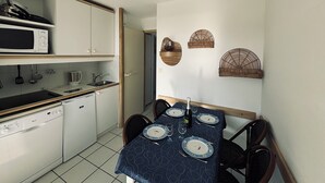 Een kleine keuken met een magnetron, koffiezetapparaat en vaatwasser. Een eettafel is gedekt voor vier personen, compleet met borden en bestek.