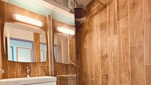 Een moderne badkamer met een wand van houtpanelen, een glazen douchecabine en een witte wastafel met spiegel.