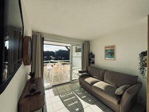 Un salón con sofá, una mesa y sillas, televisor y puerta corrediza de vidrio que da a un área exterior con mesa y sillas.