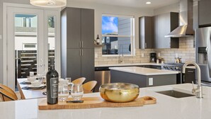 A modern kitchen with grey cabinets, stainless steel appliances, and a large island with a bowl and wine bottle. - Mountain View Home w/ King Beds & Rooftop Deck (Fort Collins)