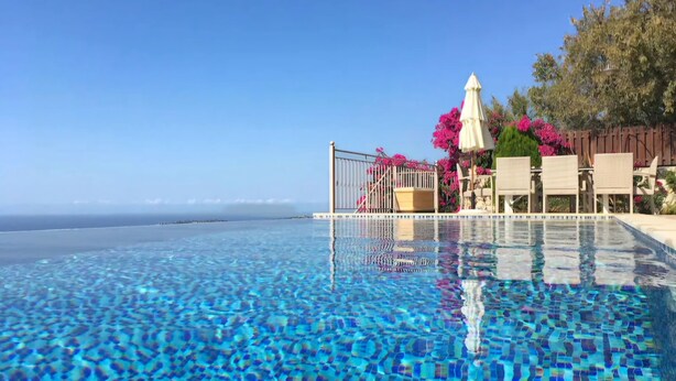 Una piscina cristallina con vista sull'oceano, circondata da posti a sedere all'aperto e fiori rosa.