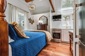 A bedroom with a large bed, a dresser, a mirror, and a kitchen area with an oven and a refrigerator. - Charming Tiny Home in Rehoboth Beach with a Water View (Rehoboth Beach)