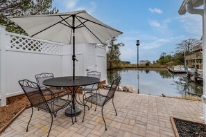 A patio with a round table and chairs, a white fence, and a view of a lake. - Charming Tiny Home in Rehoboth Beach with a Water View (Rehoboth Beach)