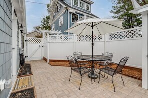 A patio with a round table and chairs, a white umbrella, and a white picket fence. - Charming Tiny Home in Rehoboth Beach with a Water View (Rehoboth Beach)