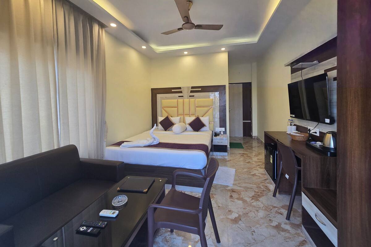 Una habitación de hotel con cama, sofá, escritorio, televisor y ventilador de techo.