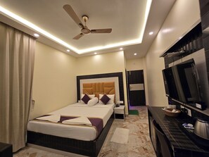 A modern hotel room with a bed, a TV, a desk, and a ceiling fan. - Elegant Beach Resort (Kanthi)