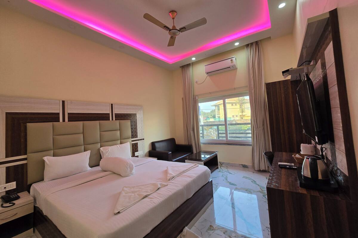Habitación de hotel con una cama grande, ventilador de techo, aire acondicionado, televisión y ventana con cortinas.