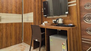 A compact room with a wooden wardrobe, a desk with a television, a chair, and a small refrigerator. - Elegant Beach Resort (Kanthi)