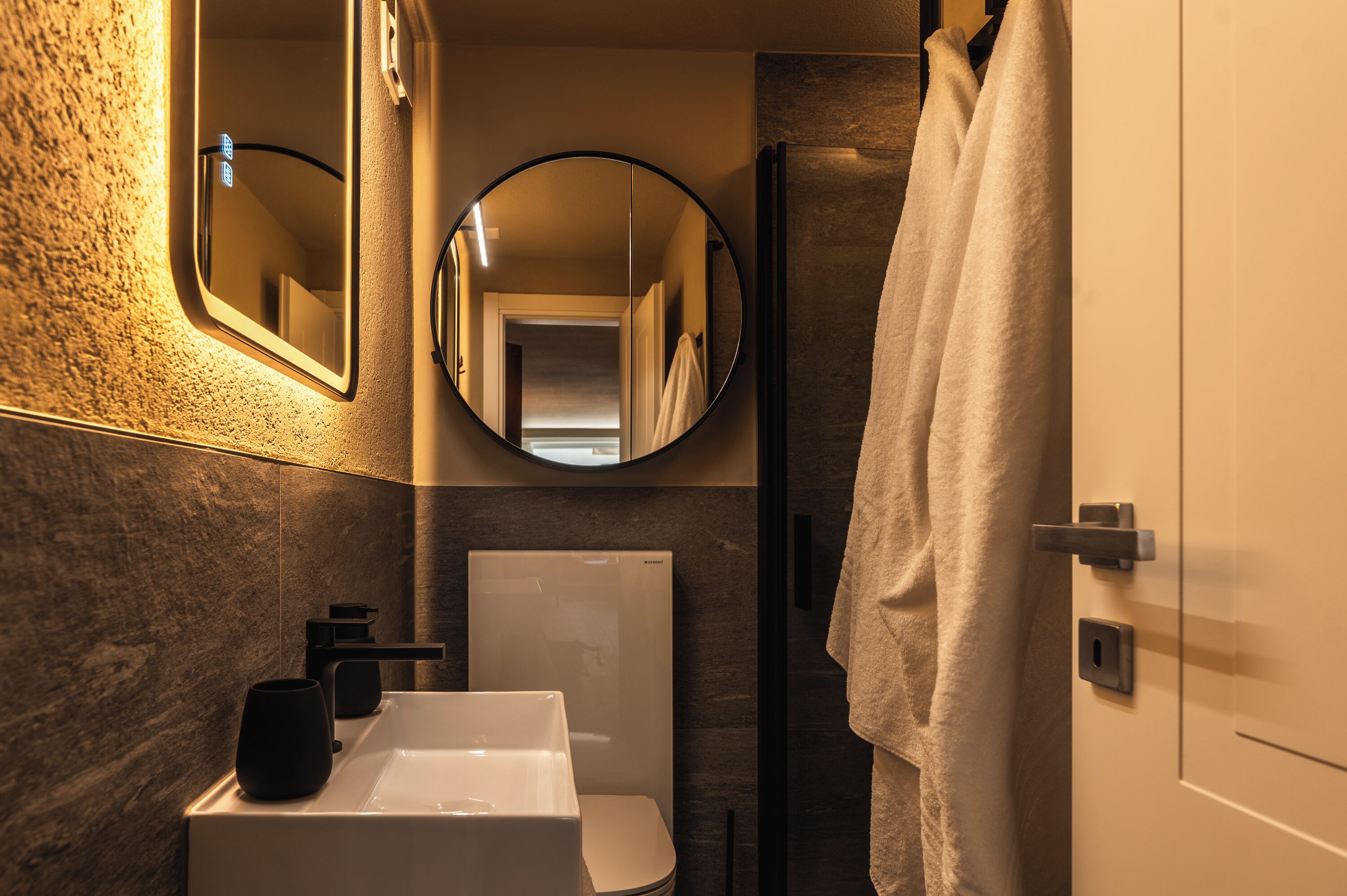 Un baño moderno con un lavamanos blanco, un grifo negro y una toalla colgada en la puerta.