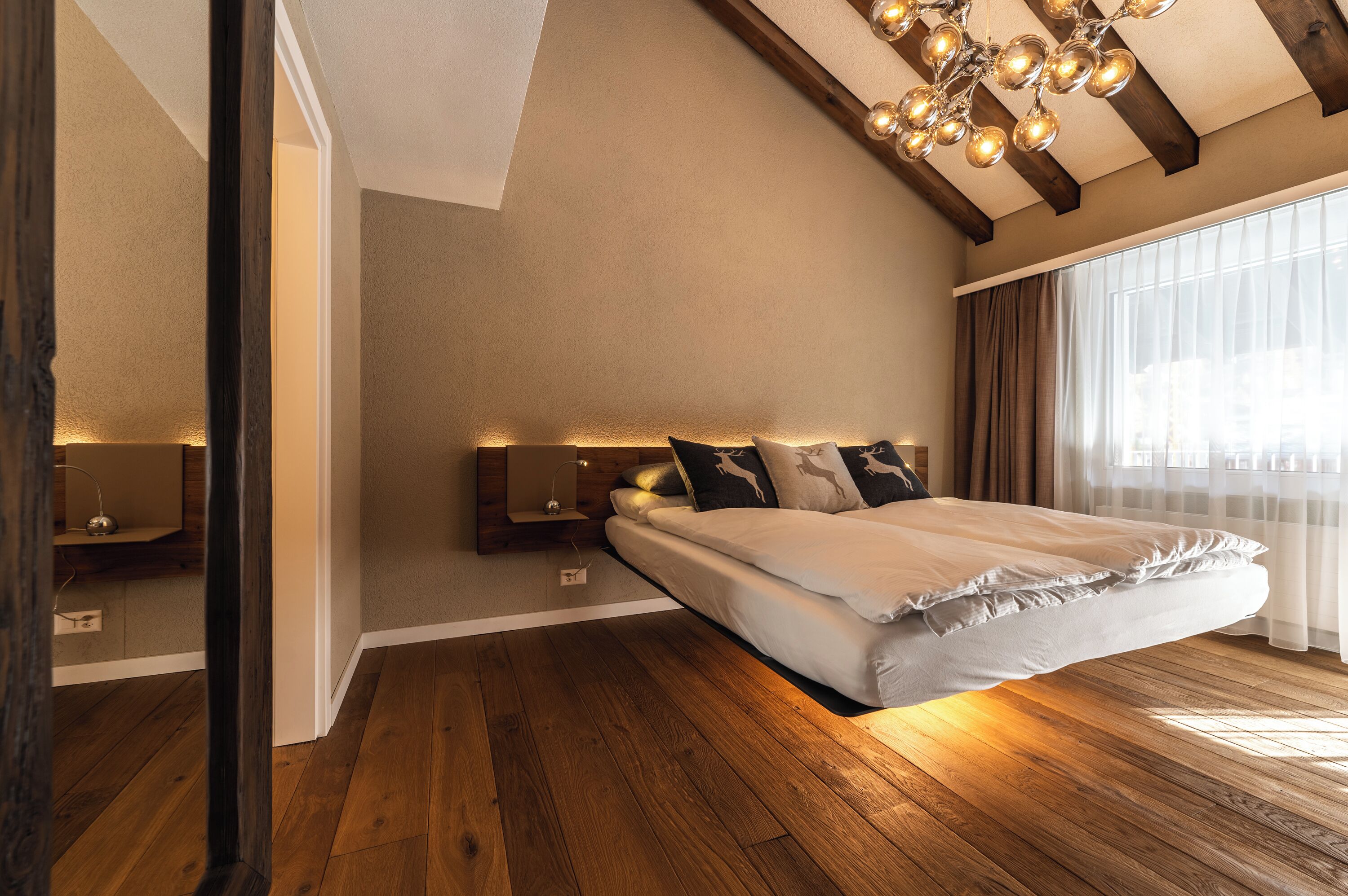 A modern bedroom with a suspended bed, wooden beams, and a chandelier.