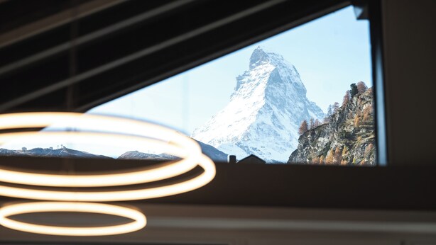 Blick auf einen Berg durch ein Fenster, mit einem modernen Interieur und runden Leuchten.