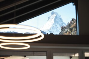 A view of a mountain through a window, with a modern interior featuring circular light fixtures. - Elfi- luxury mountain bijou (Zermatt)