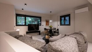 En moderne stue med sofaarrangement, fjernsyn, spisebord med stole og store vinduer.