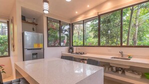 A modern kitchen with a large island, a built-in refrigerator, and a window with a view of greenery. - Surfside Apartments Mal Pais (Cóbano)