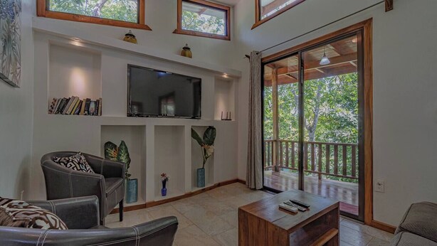 A spacious living room with a flat-screen TV, comfortable seating, and a balcony with a wooden railing. - Surfside Apartments Mal Pais (Cóbano)
