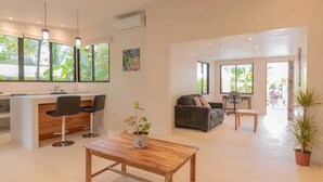 A spacious living area with a wooden coffee table, a sofa, and a kitchen area with bar stools. - Surfside Apartments Mal Pais (Cóbano)