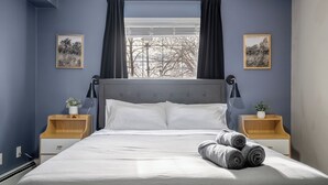 A neatly made bed with white linens, two bedside tables with lamps, and two framed pictures on the walls. - Spacious Riverfront DT Condo: 3 Beds, AC, Heated Parking, Stampede & Saddledome (Calgary)