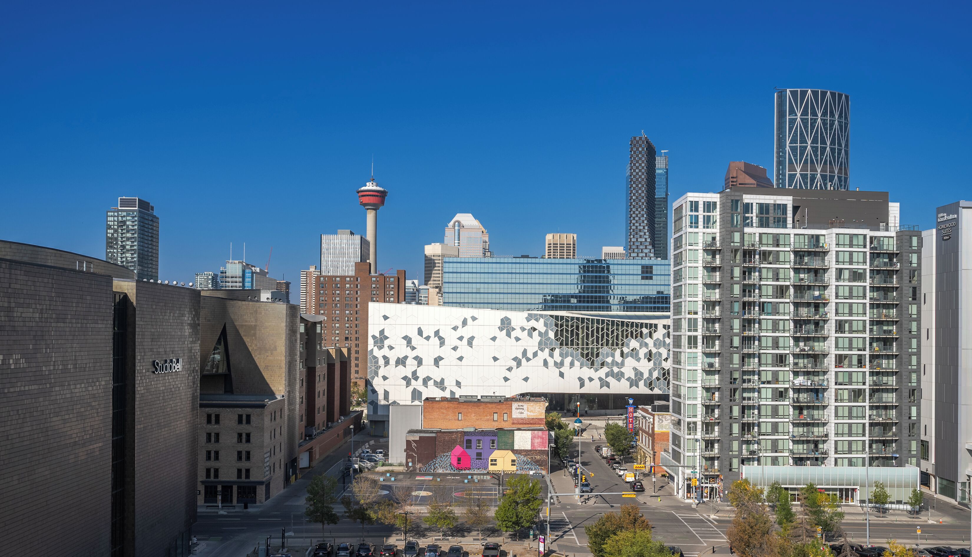 Un quartier urbain moderne qui présente un mélange de bâtiments commerciaux et résidentiels, notamment un bâtiment blanc remarquable avec une façade géométrique et une haute tour surmontée d’une flèche.