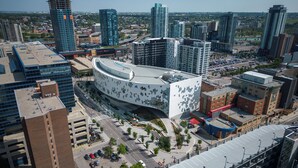 A modern building with a curved facade, surrounded by high-rise buildings and a parking area. - Spacious Riverfront DT Condo: 3 Beds, AC, Heated Parking, Stampede & Saddledome (Calgary)