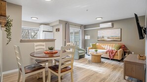 A modern living space with a dining area, a sofa, and a TV mounted on the wall. - Spacious Riverfront DT Condo: 3 Beds, AC, Heated Parking, Stampede & Saddledome (Calgary)