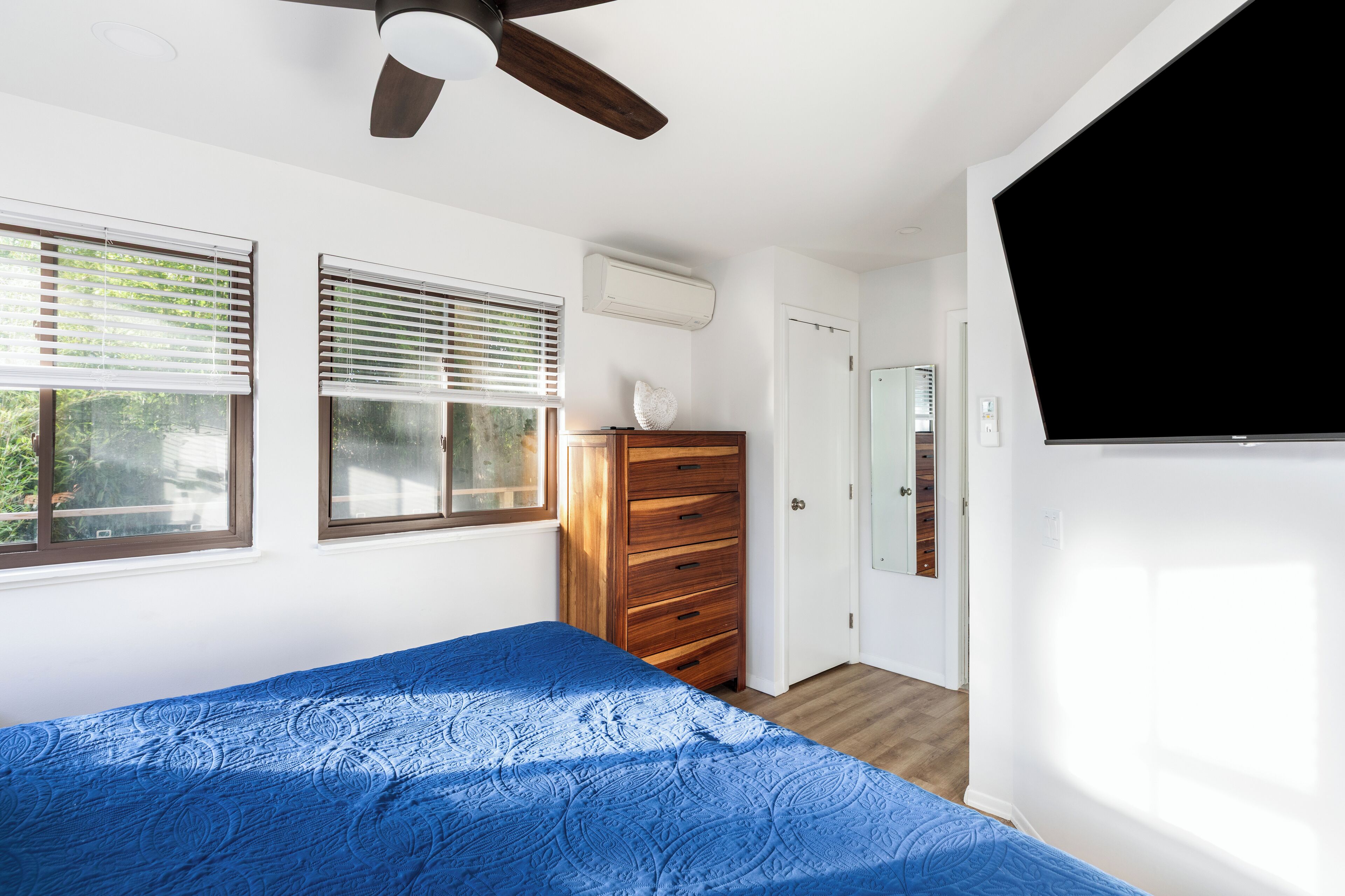 Une chambre à coucher avec un lit, une commode en bois, un ventilateur de plafond et un téléviseur.