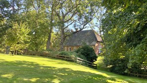 A thatched-roof cottage surrounded by lush greenery and a wooden fence.