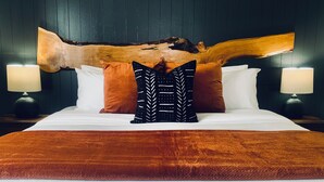 Een net opgemaakt bed met witte lakens, een groot houten decoratiestuk en twee nachtkastjes met lampen.