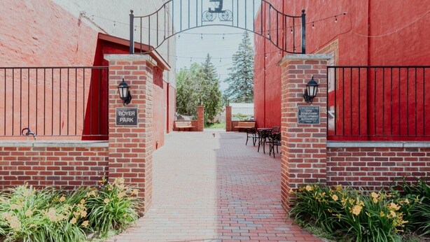 A brick pathway leading to a building with a red exterior, a sign reading 'BOYER PARK,' and a metal gate with a bicycle symbol.