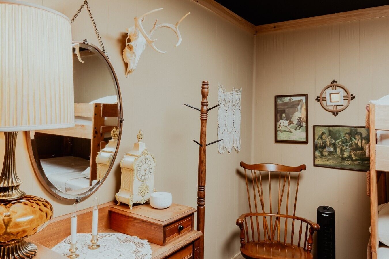 Une chambre avec un lit superposé, une chaise en bois, une petite table avec une lampe, une horloge et des décorations murales, notamment un crâne et des tableaux encadrés.