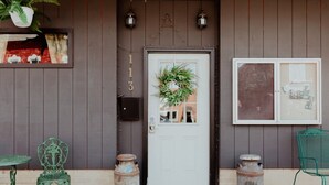 A wooden door with a number '113' above it, a white doorbell, and a small window with a plant.
