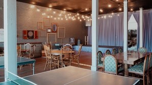 A room with ping pong tables, wooden chairs, and a dartboard on the wall.